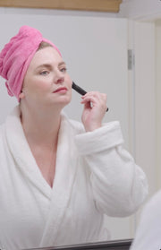 Woman applying makeup wearing a pink microfiber Turbie twist hair towel